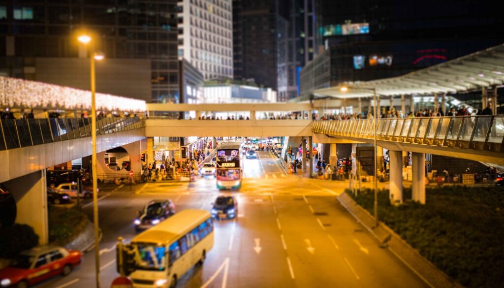 Tilt shift of busy street at night with overhead footbridges