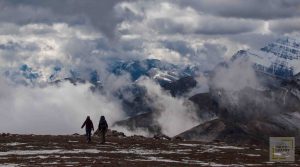 Man and woman walking towards edge of a plateau in mountains with clouds rising and snow