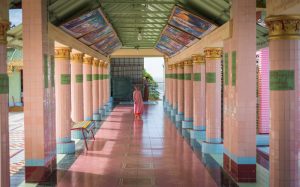 Female monk standing in temple in corridor with large pink pillars on either side