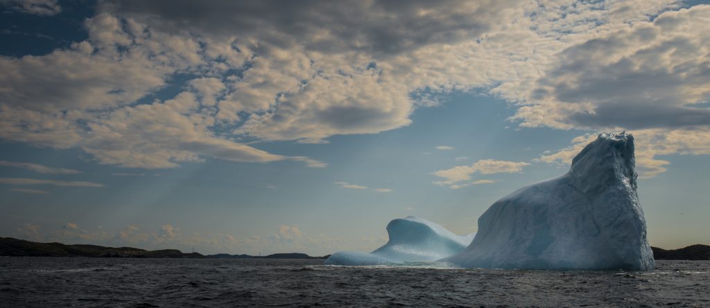 Iceberg floating in ocean with streams of sunlight coming through clouds